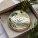 A decorative ornament in a box, featuring a scenic landscape of Half Moon Bay, California.