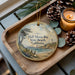 A wooden tray with a decorative ornament featuring a scenic image of Half Moon Bay State Beach, California, and a candle on a table.