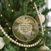 A round ornament hanging on a Christmas tree, featuring a scenic landscape with birds, a bridge, and a body of water.