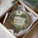 A round ornament with a scenic image of a pond and trees, hanging from a string inside a box.