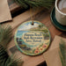 A decorative ornament with a tropical beach scene, featuring palm trees, flowers, and a body of water, hangs on a wooden surface.