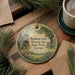 A round ornament with a painting of a farm and a house, hanging on a wooden surface.