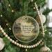 A round ornament hanging on a Christmas tree, featuring a scenic image of a historic farm and a house surrounded by trees and flowers.