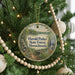 A round ornament hanging on a Christmas tree, featuring a scenic landscape with a bridge and trees.