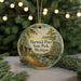A round ornament with a painting of a cabin and a forest scene, hanging from a string.