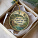 A round ornament with a tropical island scene and text, placed in a box with a white tissue paper lining.