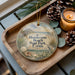 A round ornament with a beach scene and the text "Henderson Beach State Park, Florida" is displayed on a wooden tray, accompanied by pine cones and a lit candle.
