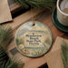 A round ornament with a beach scene and the text "Henderson Beach State Park, Florida" hangs on a wooden surface, surrounded by pine branches and a cup of coffee.