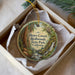 A round ornament with a painting of a forest scene, featuring a waterfall and trees, is displayed in a box.