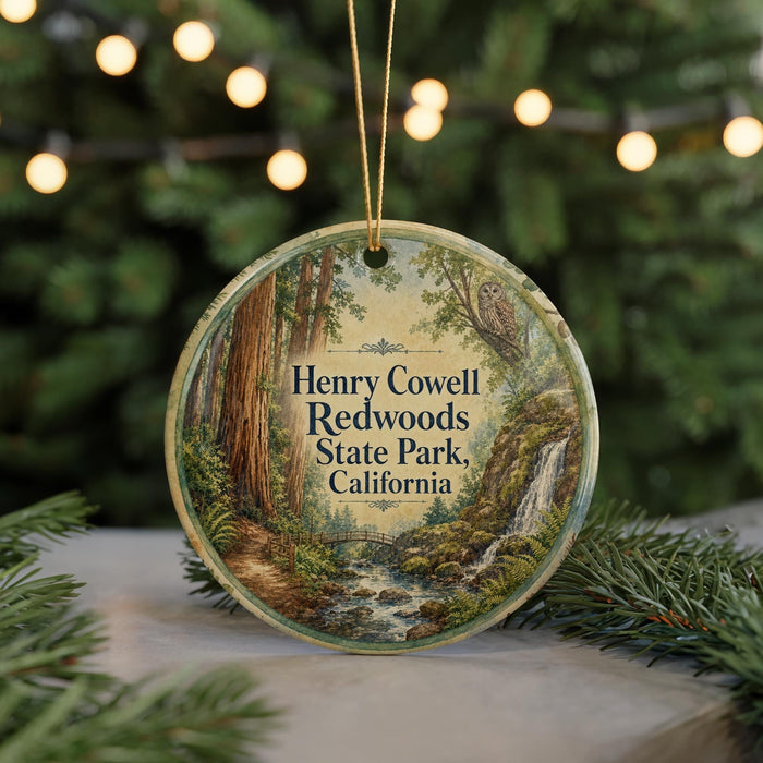 A circular ornament with a painting of a forest scene, featuring a waterfall and trees, hangs in front of a blurred background with Christmas lights.