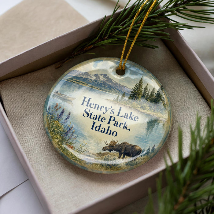 A decorative ornament in a box, featuring a moose and a scenic landscape with mountains and water.