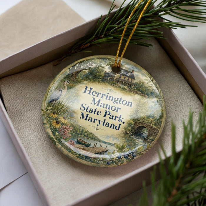 A decorative ornament in a box, featuring a scenic landscape with a house, trees, and a body of water.