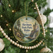 A round ornament hanging on a Christmas tree, featuring a scenic landscape with a waterfall and pine trees.