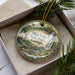 A decorative ornament with a scenic image of High Falls State Park, Georgia, displayed in a box with pine branches.