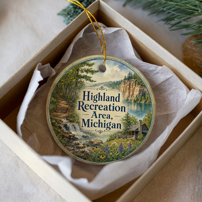 A decorative ornament in a box, featuring a scenic landscape with a waterfall, trees, and a cabin.