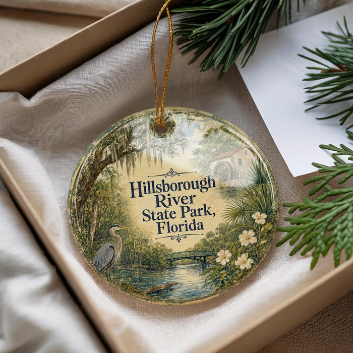 A decorative ornament with a bird and a river scene, placed in a box with pine branches.