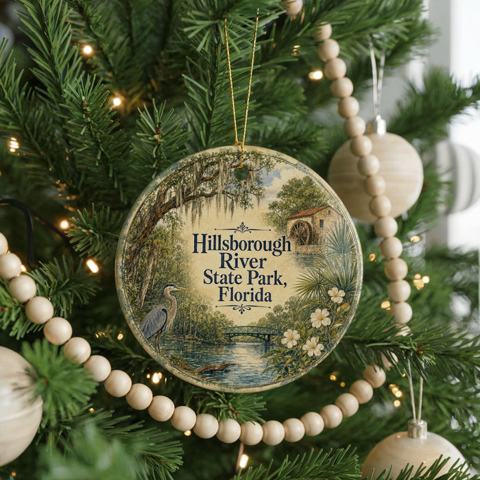 A round ornament hanging on a Christmas tree, featuring a scenic image of Hillsborough River State Park, Florida.