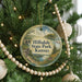 A round ornament hanging on a Christmas tree, featuring a scenic landscape with a lake and mountains.