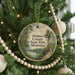 A round ornament hanging on a Christmas tree, featuring a scenic image of a park with a lake and a bird.