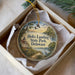 A round ornament in a box, featuring a scenic landscape with a lighthouse, trees, and a body of water.