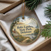 A round ornament with a scenic landscape of a lighthouse, a house, and a bird, hanging from a string.