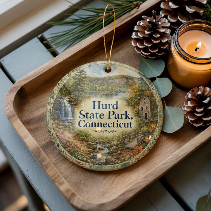 A wooden tray with a decorative ornament featuring a scenic image of Hurd State Park in Connecticut, accompanied by pine cones and a lit candle.