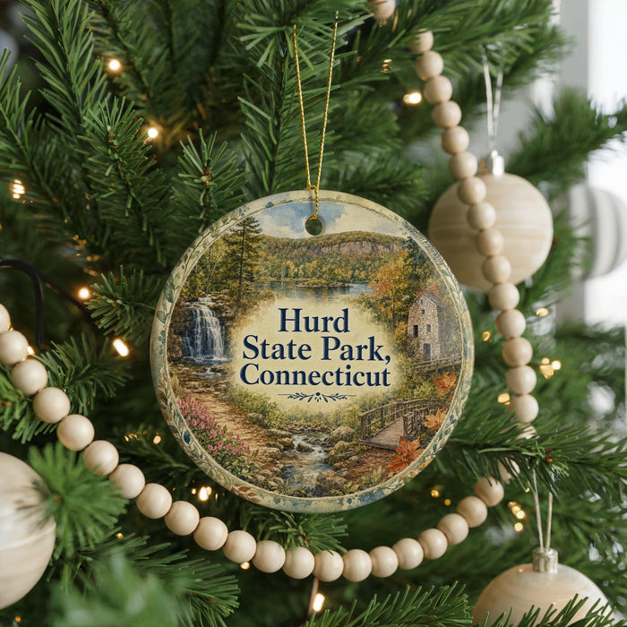 A round ornament hanging on a Christmas tree, featuring a scenic landscape with a waterfall and a bridge.