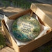A decorative ornament in a box, featuring a scenic image of a manatee surrounded by lush greenery and a bridge, with the text "Ichetucknee Springs State Park, Florida" printed on it.