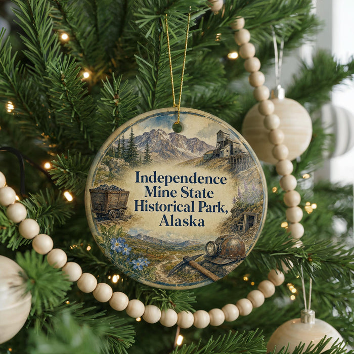 A round ornament hanging on a Christmas tree, featuring an illustration of Independence Mine and Historical Park in Alaska.