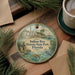 A decorative ornament featuring a tropical scene with a bird, palm trees, and a building, hanging on a wooden surface.