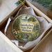 A round ornament with a scenic landscape of Interlochen State Park, Michigan, displayed in a box with a white tissue paper lining.