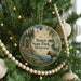 A circular ornament hanging on a Christmas tree, featuring a moose and a scenic landscape with a river and trees.