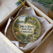 A decorative ornament in a box, featuring a scenic landscape with a river, trees, and a bridge.