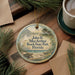A round ornament with a beach scene and a bird on a sandy beach, surrounded by pine branches and a cup of coffee on a wooden surface.