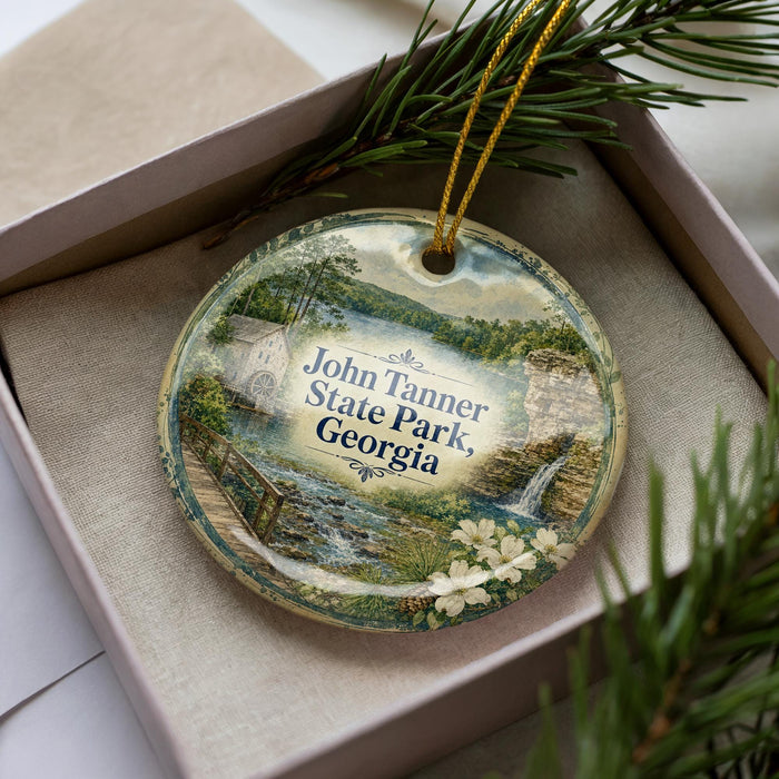 A decorative ornament in a box, featuring a scenic landscape with a bridge, water, and flowers.