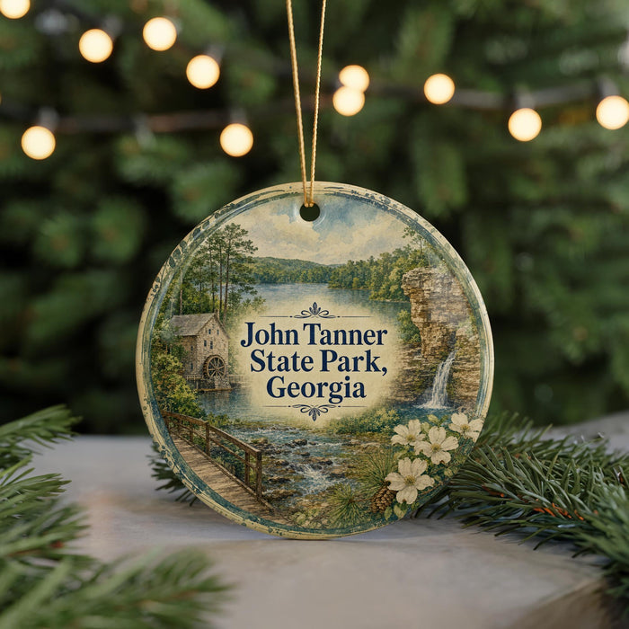 A round ornament featuring a scenic landscape with a river, bridge, and waterfall, surrounded by greenery and flowers, with the text "John Tanner State Park, Georgia" displayed prominently.