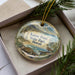 A decorative ornament in a box, featuring a scenic image of Kaena Point State Park in Hawaii.
