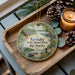 A decorative ornament featuring a scenic view of Kenlake State Resort Park, Kentucky, with a candle and pine cones on a wooden tray.
