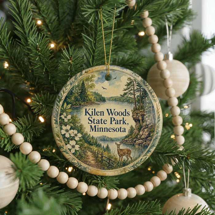 A round ornament hanging on a Christmas tree, featuring a scenic landscape with a lake, trees, and a deer.