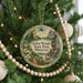 A round ornament hanging on a Christmas tree, featuring a scenic landscape with a lake, trees, and a deer.