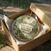 A decorative ornament in a wooden box, featuring a scenic landscape with a deer and trees, with the text "Kilen Woods State Park, Minnesota" printed on it.