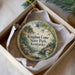 A decorative ornament in a box, featuring a scenic landscape with a river, bridge, and trees.