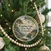 A round ornament hanging on a Christmas tree, featuring a scenic landscape with a river and trees.