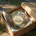 A decorative ornament in a box, featuring a scenic landscape with mountains, waterfalls, and lush vegetation.
