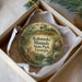 A decorative ornament in a box, featuring a deer and a landscape scene with mountains, trees, and a pond.