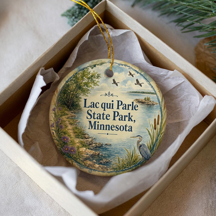 A decorative ornament in a box, featuring a scenic landscape with a lake, trees, and birds.