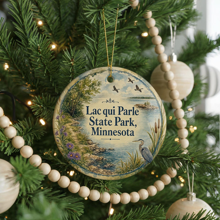 A round ornament hanging on a Christmas tree, featuring a scenic landscape with a lake, trees, and birds.