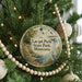 A round ornament hanging on a Christmas tree, featuring a scenic landscape with a lake, trees, and birds.