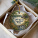 A decorative ornament in a box, featuring a scenic landscape with a lake, a castle, and a deer.