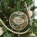 A round ornament hanging on a Christmas tree, featuring a scenic landscape with a lake, forest, and waterfall.
